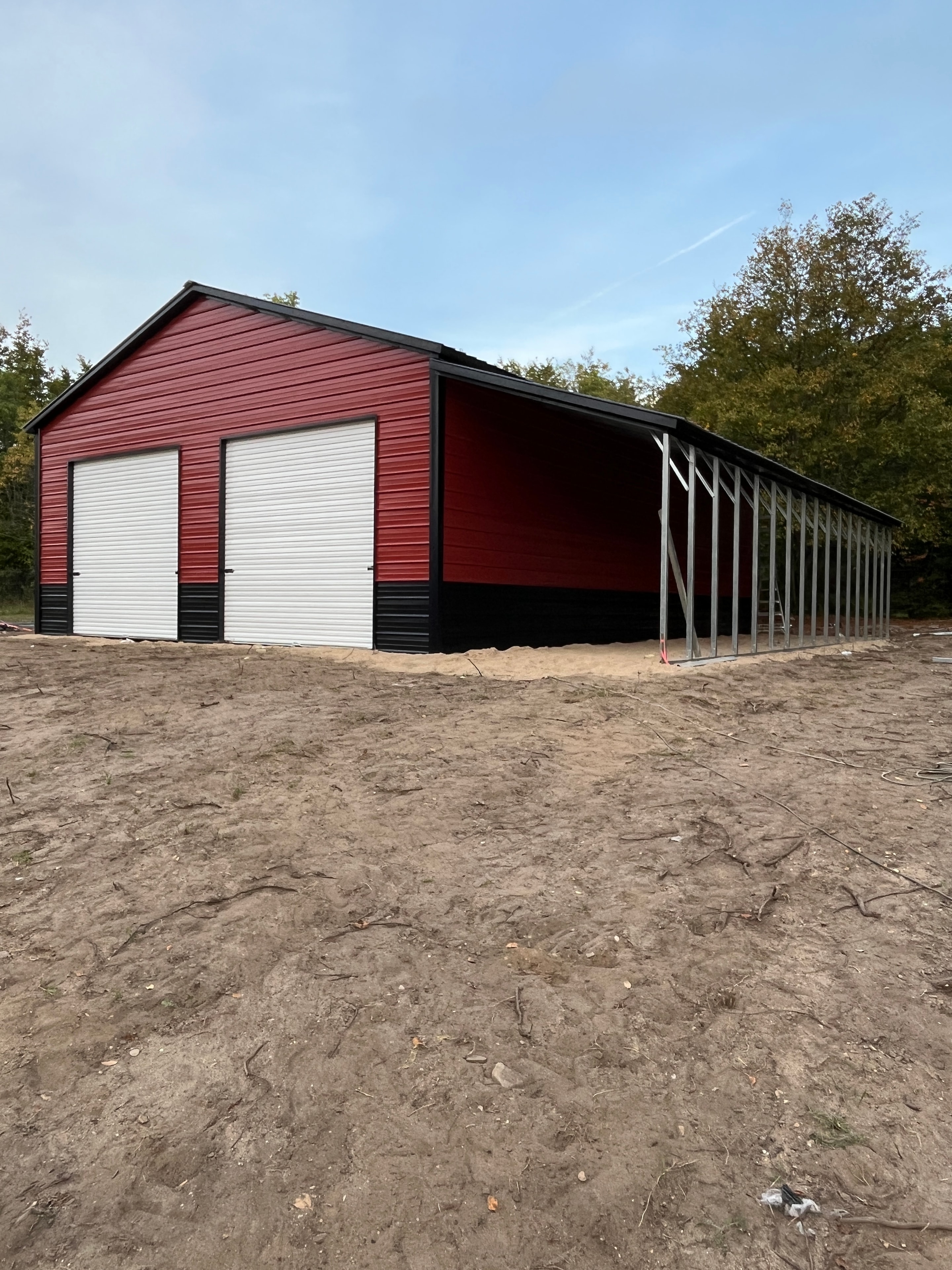 Barn red and white metal workshop under construction with exposed steel framing and roll-up door openings