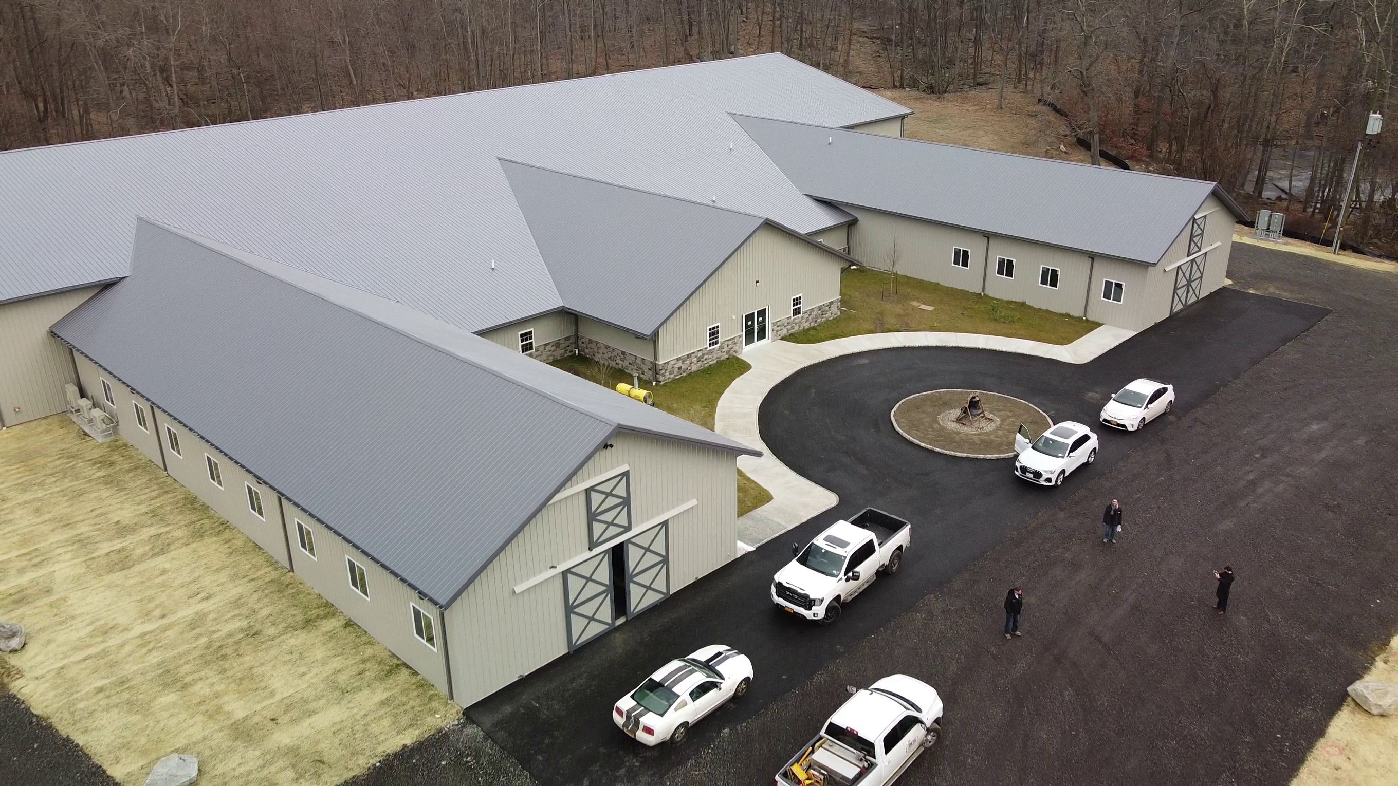 Aerial view of a large gray metal barndominium complex with multiple buildings and circular driveway