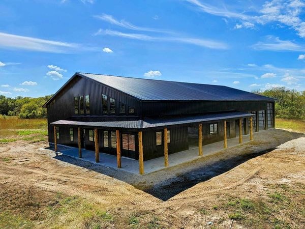 Black metal barndominium with covered wrap-around porch and wood post accents