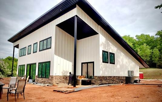 Modern white barndominium with black trim, stone wainscot, and large windows under construction