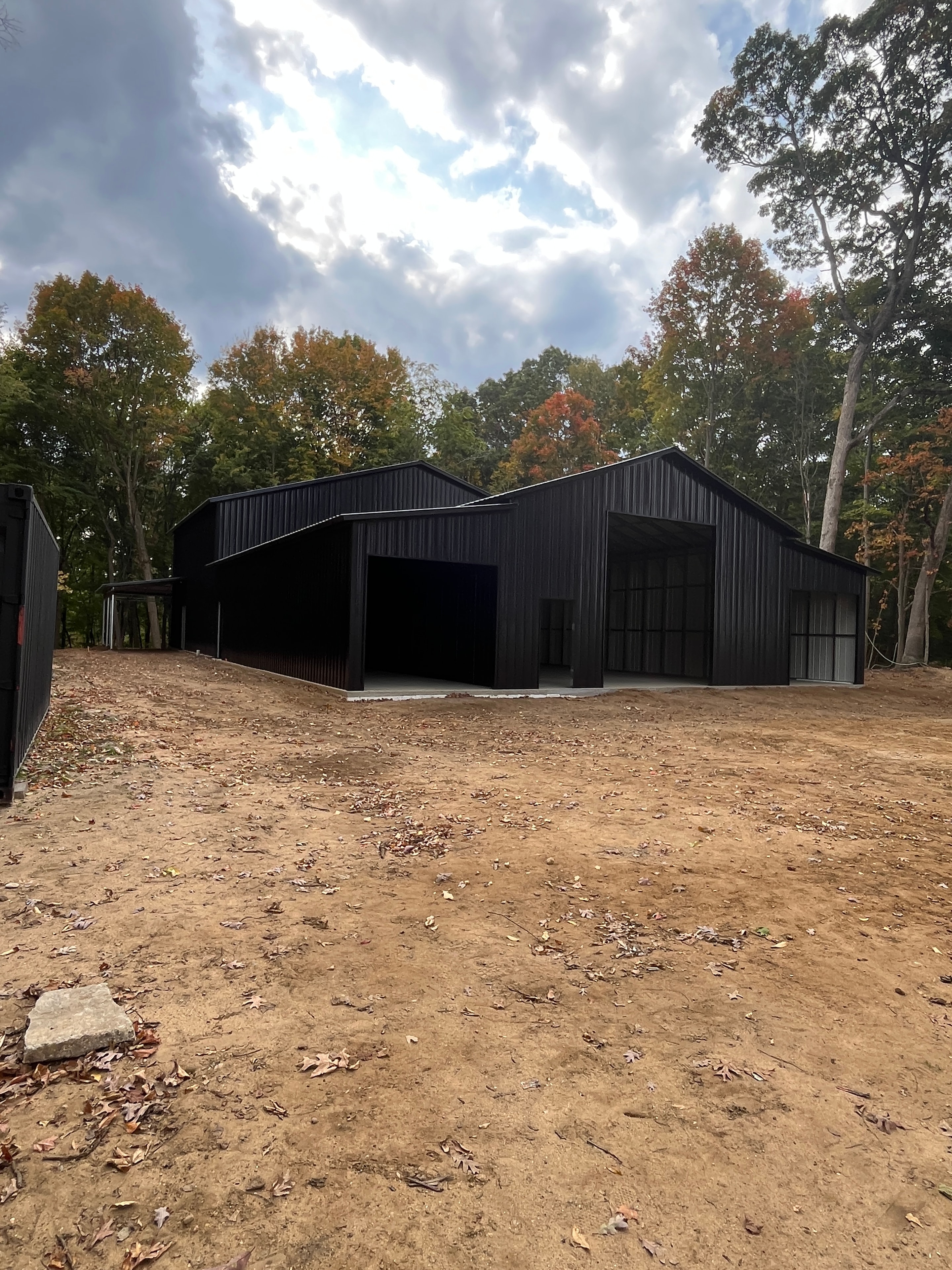 Black metal barndominium structure with large windows in a wooded fall setting