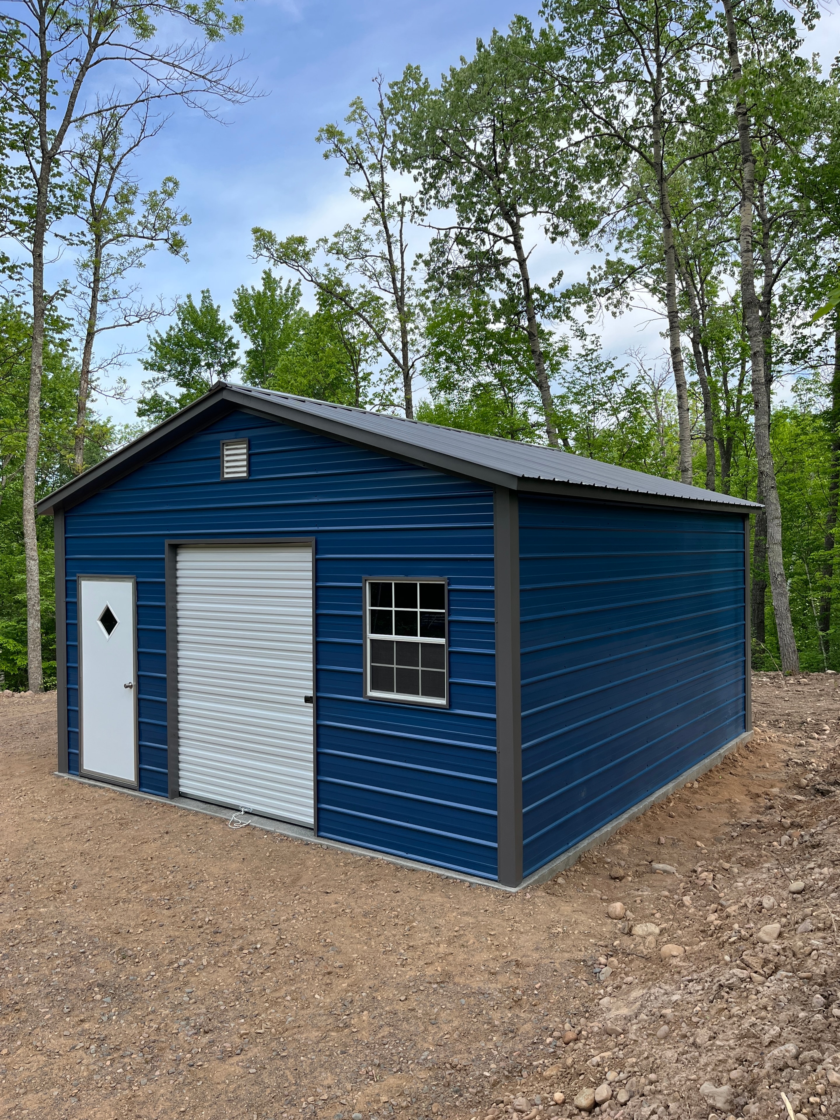 Blue metal garage with vertical siding, roll-up door, walk-in door, and window