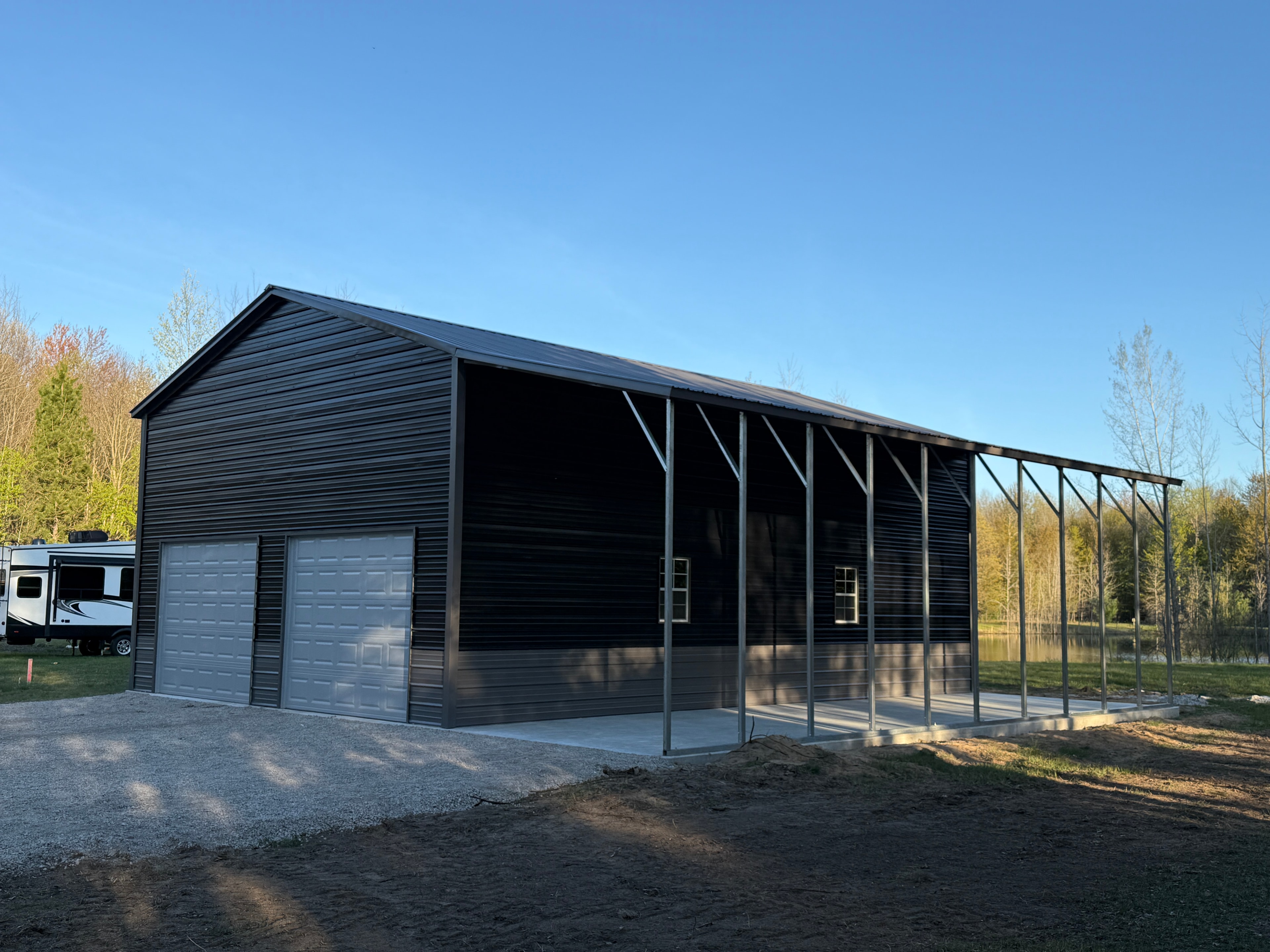 Large charcoal metal barn with lean-to overhang, roll-up door, windows, and concrete pad