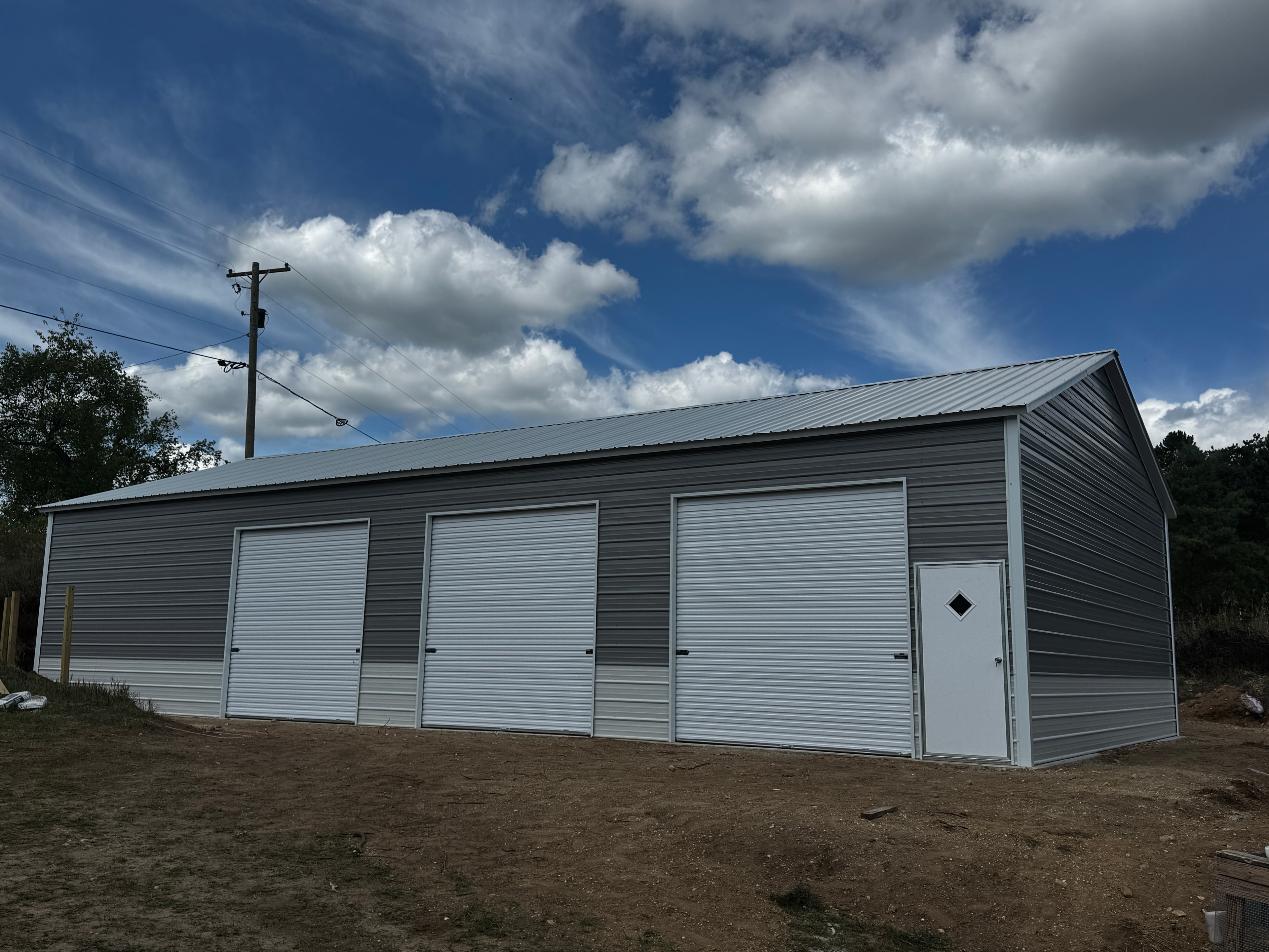 Large charcoal gray metal workshop with three roll-up doors and a walk-in door on eave side