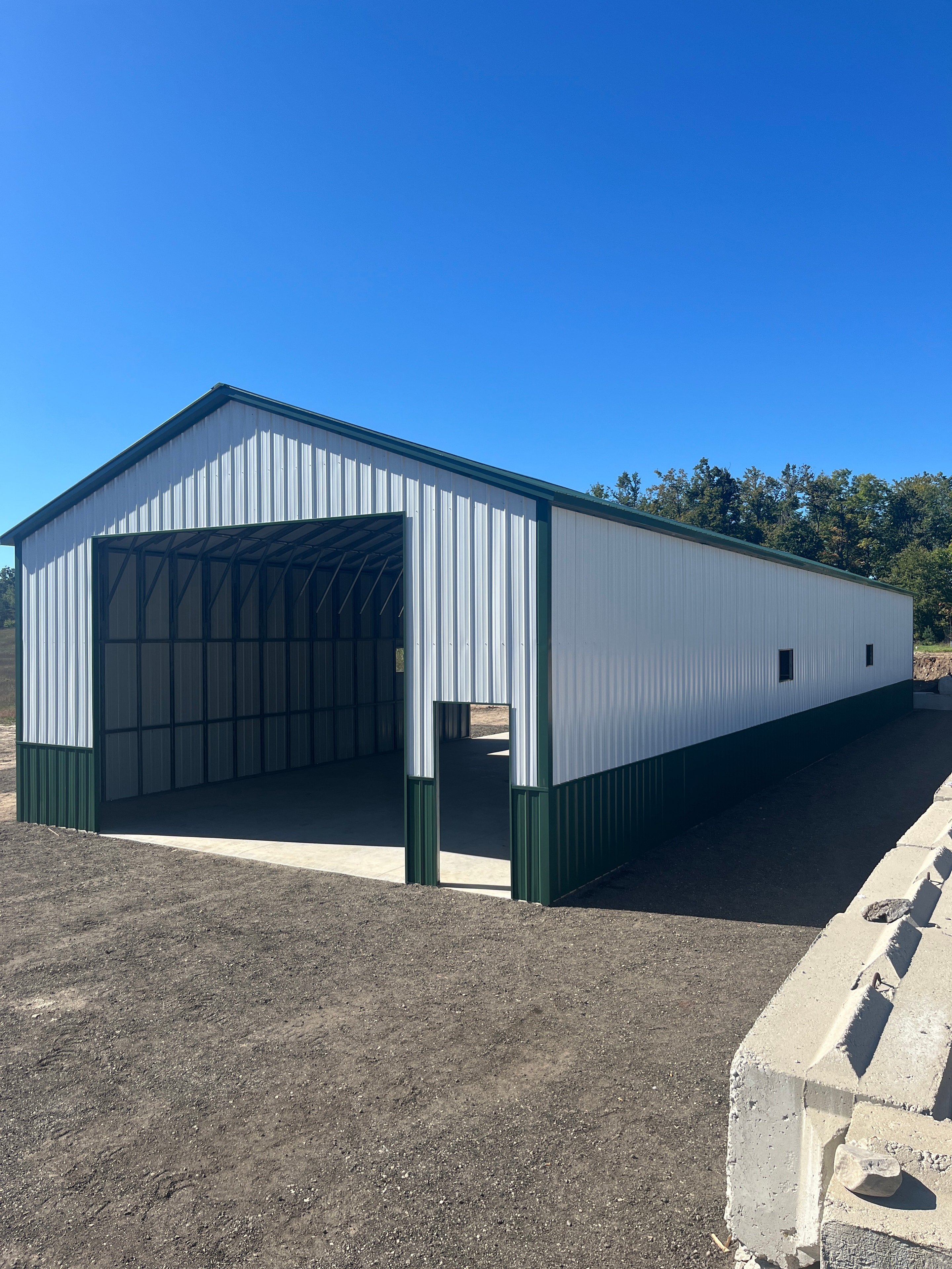 Galvalume metal workshop with dark green trim, large roll-up door, and windows on a concrete pad