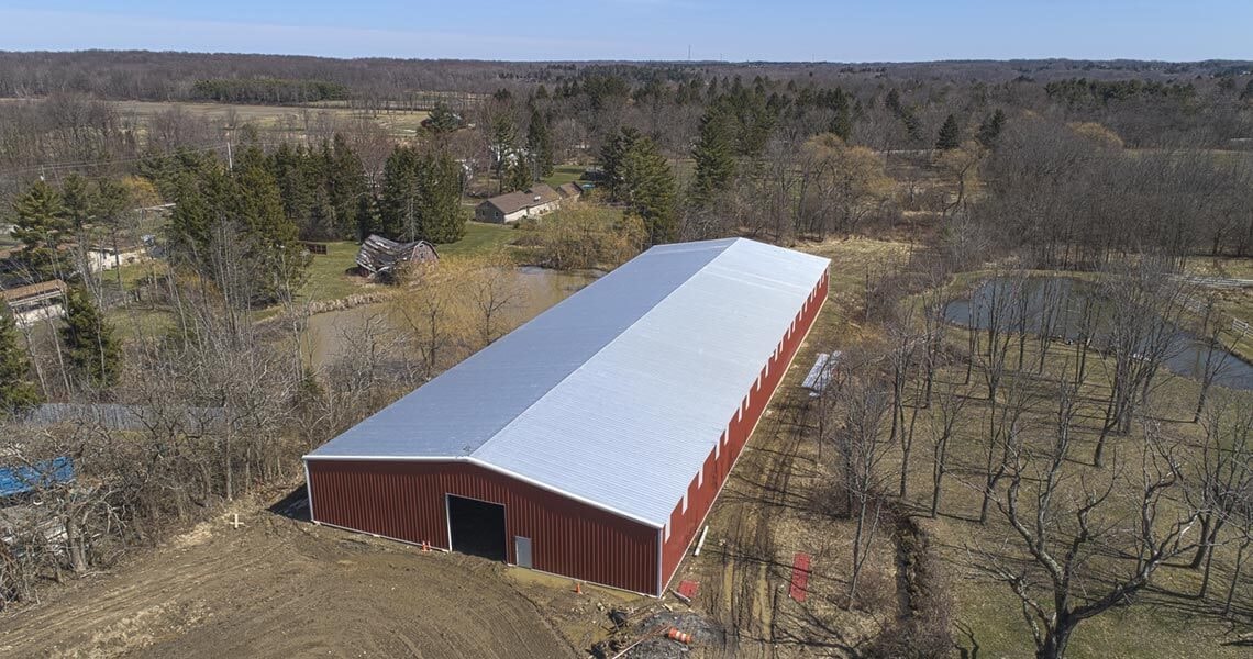 Aerial view of a large red rigid-frame agricultural building with white roof