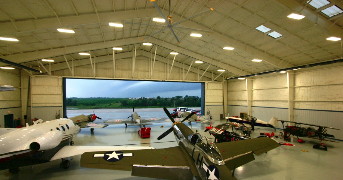 Interior of a rigid-frame aircraft hangar with vintage planes and panoramic door opening