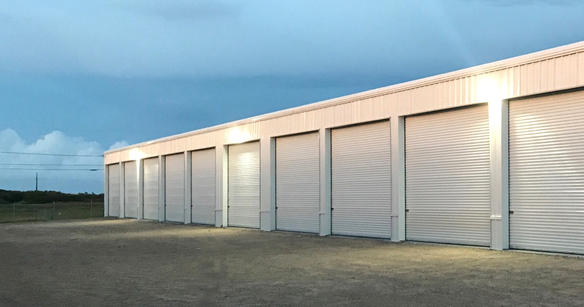 White rigid-frame storage building with multiple roll-up doors lit at dusk