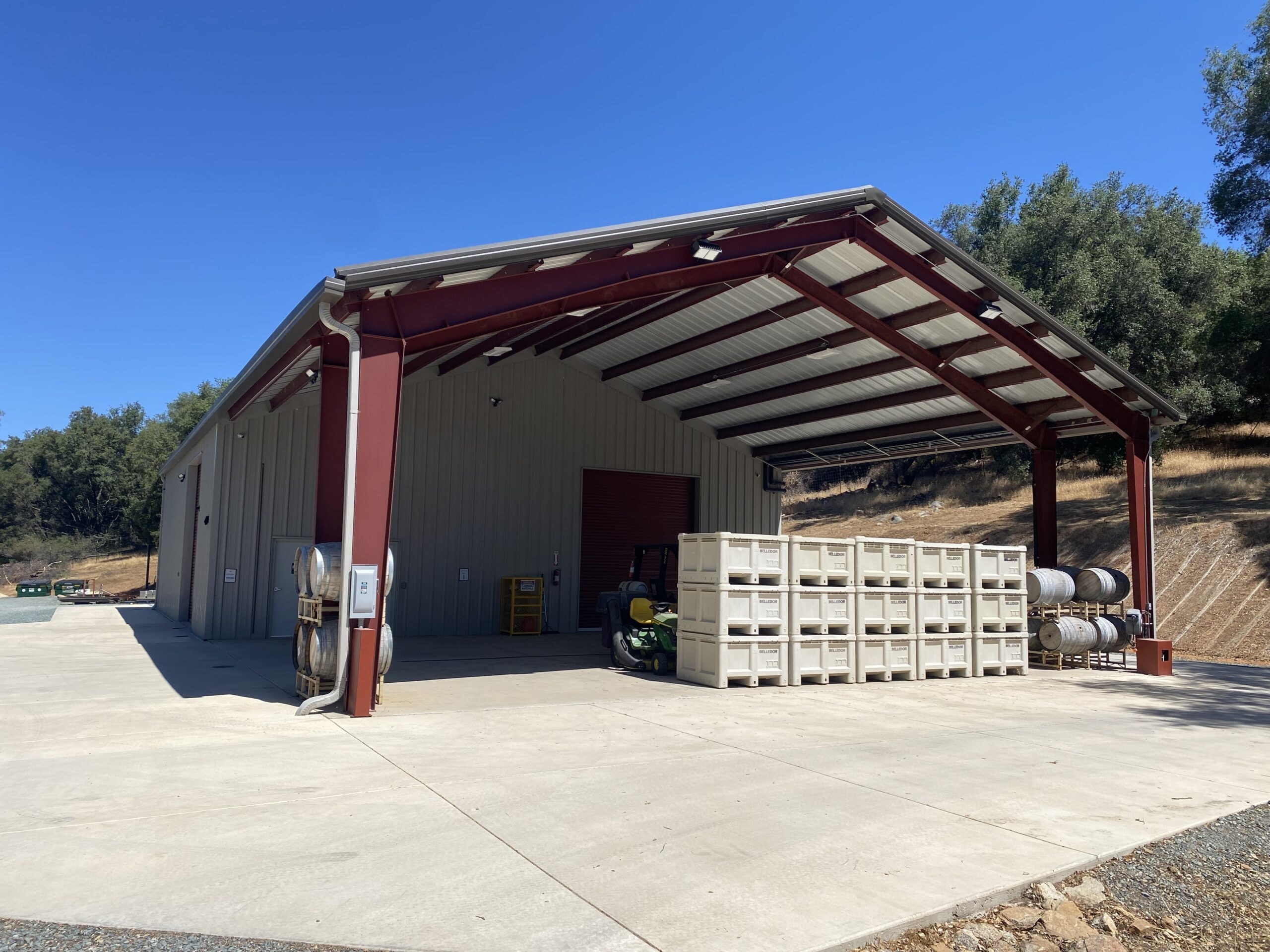 Tan rigid-frame agricultural building with red steel framing and open lean-to overhang