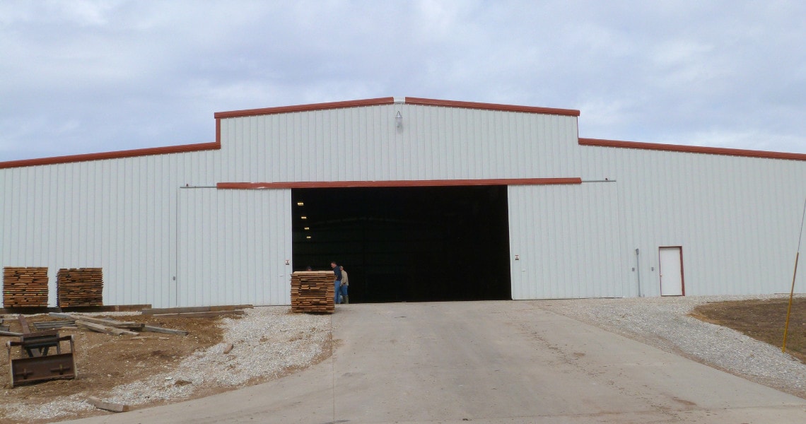 Large white rigid-frame building with wide open bay doors and red trim
