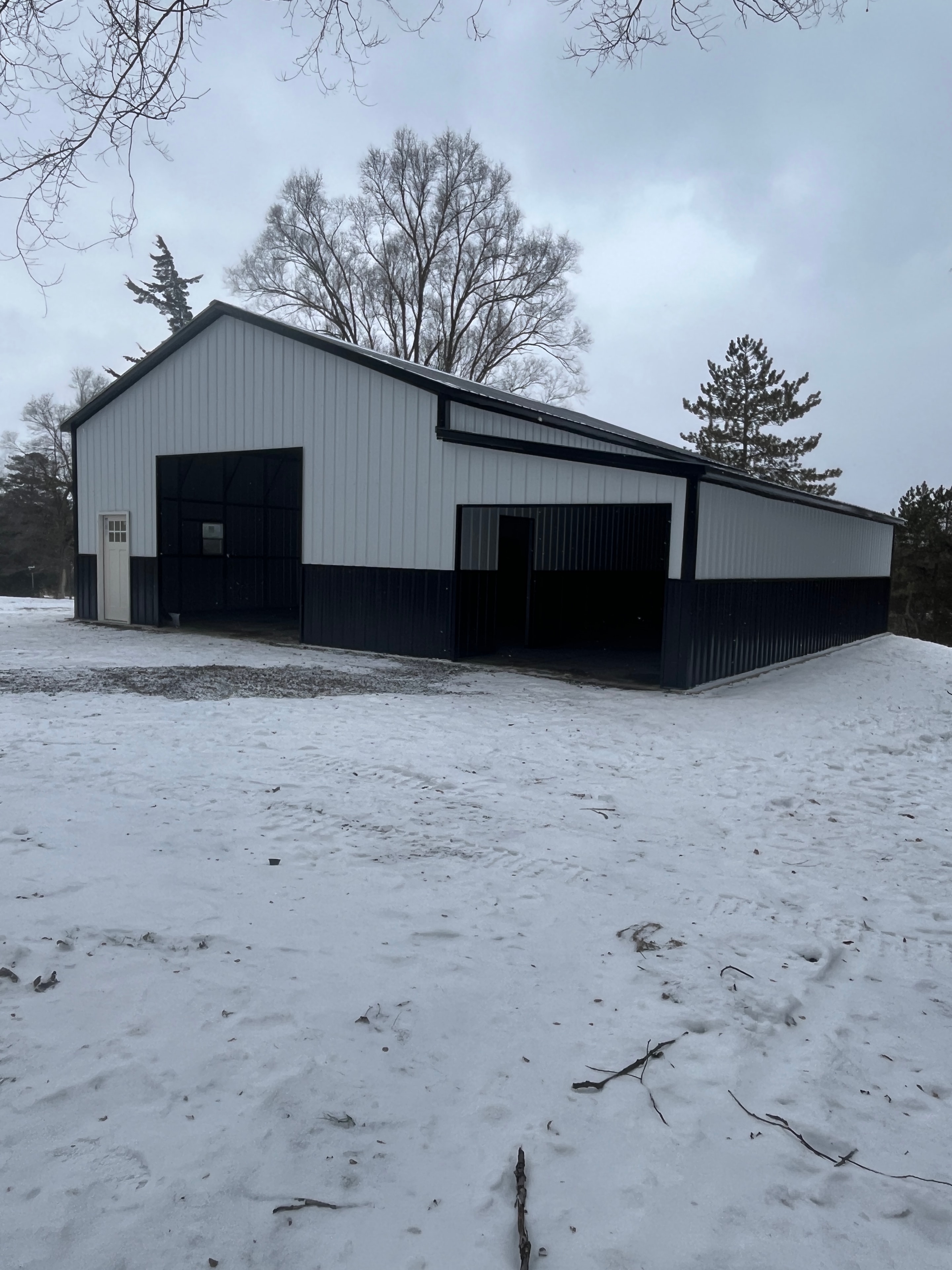 White metal garage with black trim and lean-to overhang in a snowy landscape